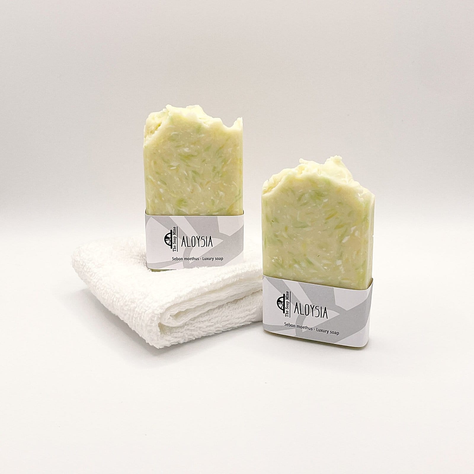 Two bars of white and green Aloysia handmade soap and a white facecloth