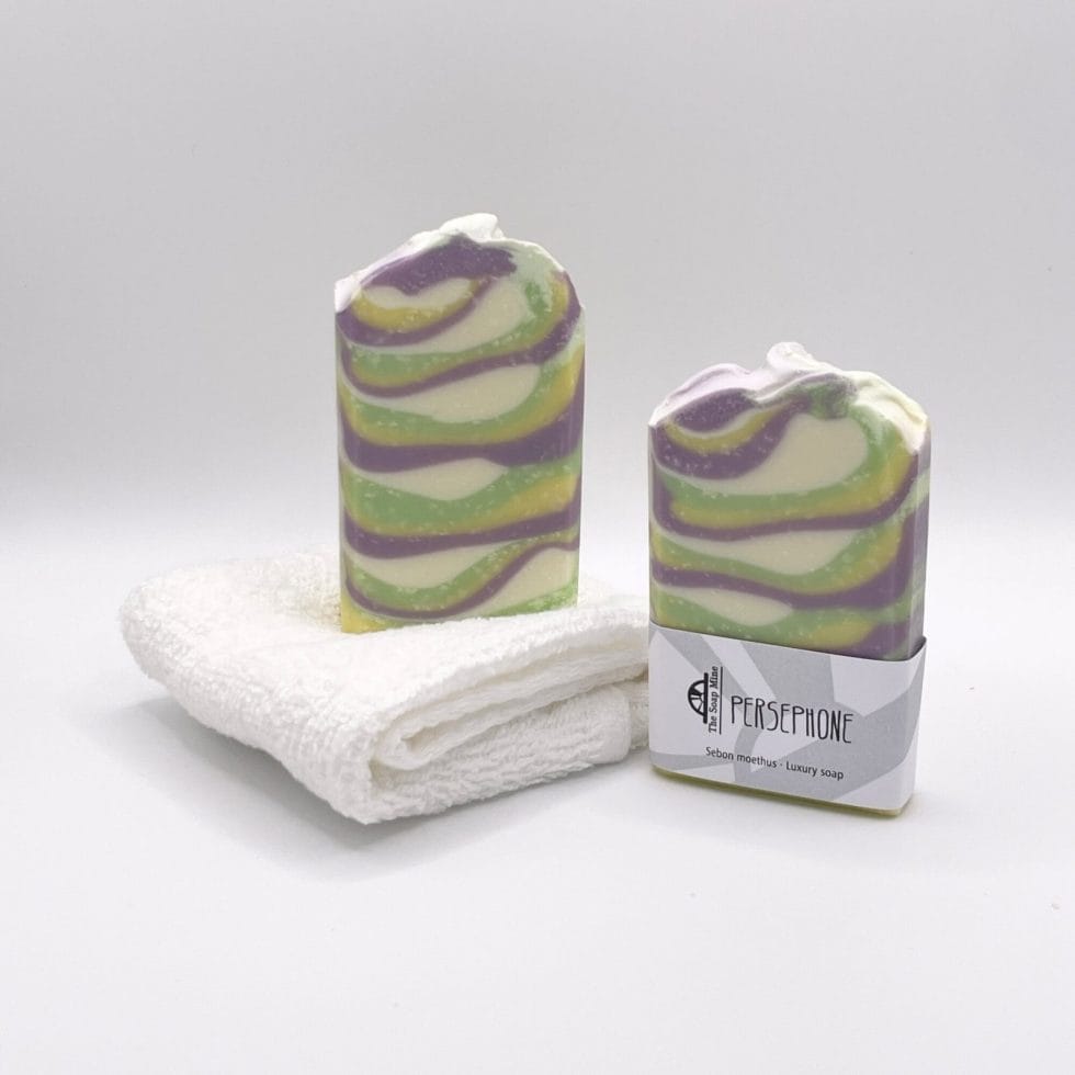 Two bars of yellow, purple, white and green Persephone handmade soap and a  facecloth
