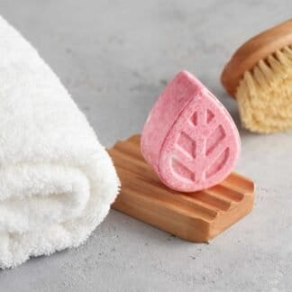 A bar of pink solid shampoo, a soap dish and a white towel